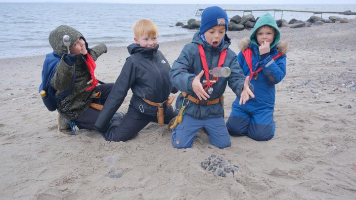 Fire minispejdere bagved en lille pingvinformet i sand, de smiler og fjoller.